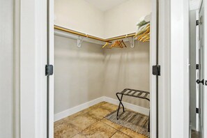 Um closet amplo com uma barra de madeira, uma estante de metal e uma prateleira pequena.