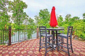 Une terrasse avec une table et des chaises, un parasol rouge, et une vue sur une étendue d’eau et des arbres.