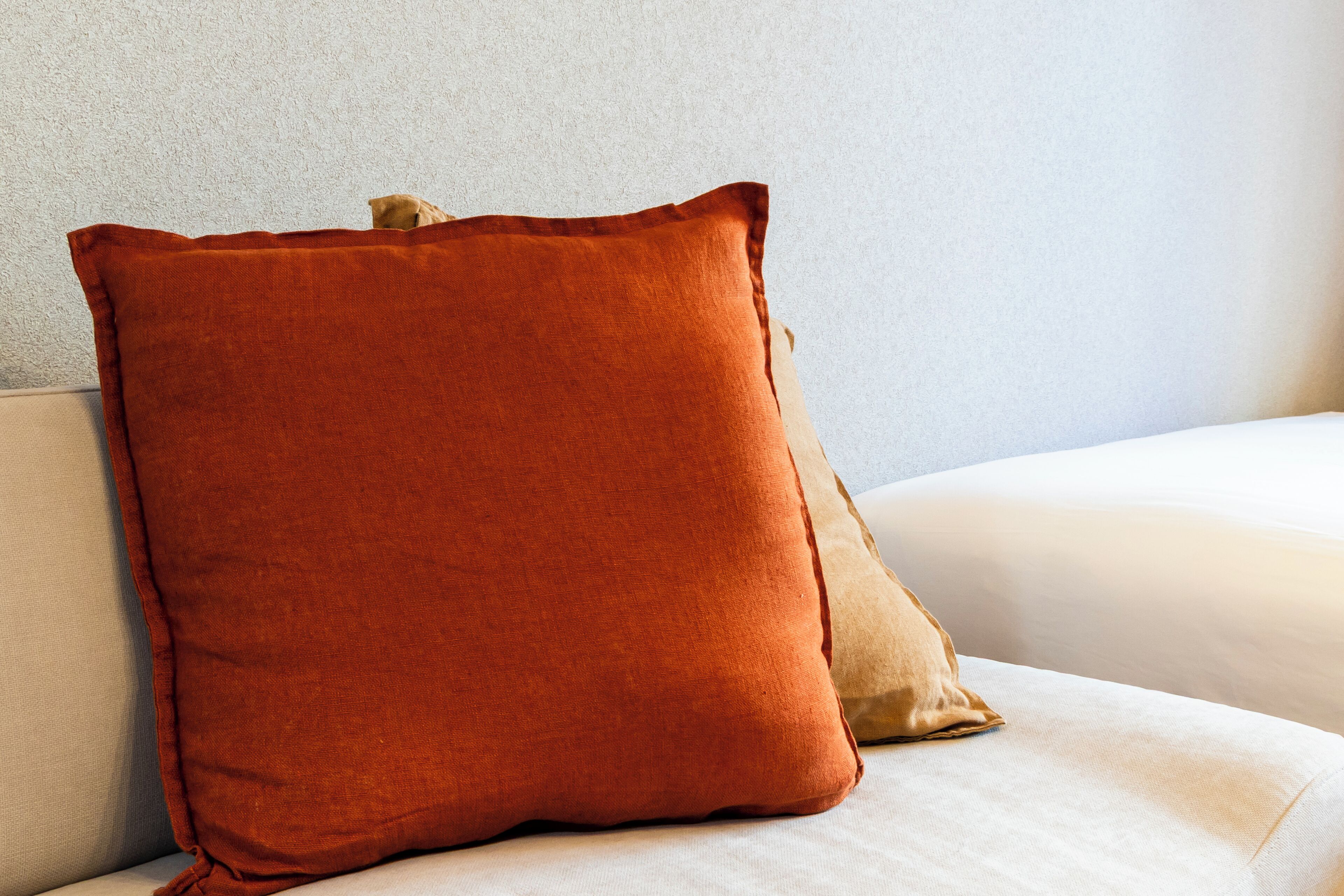 Una cama con colchón blanco y dos almohadas, una roja y otra beige.