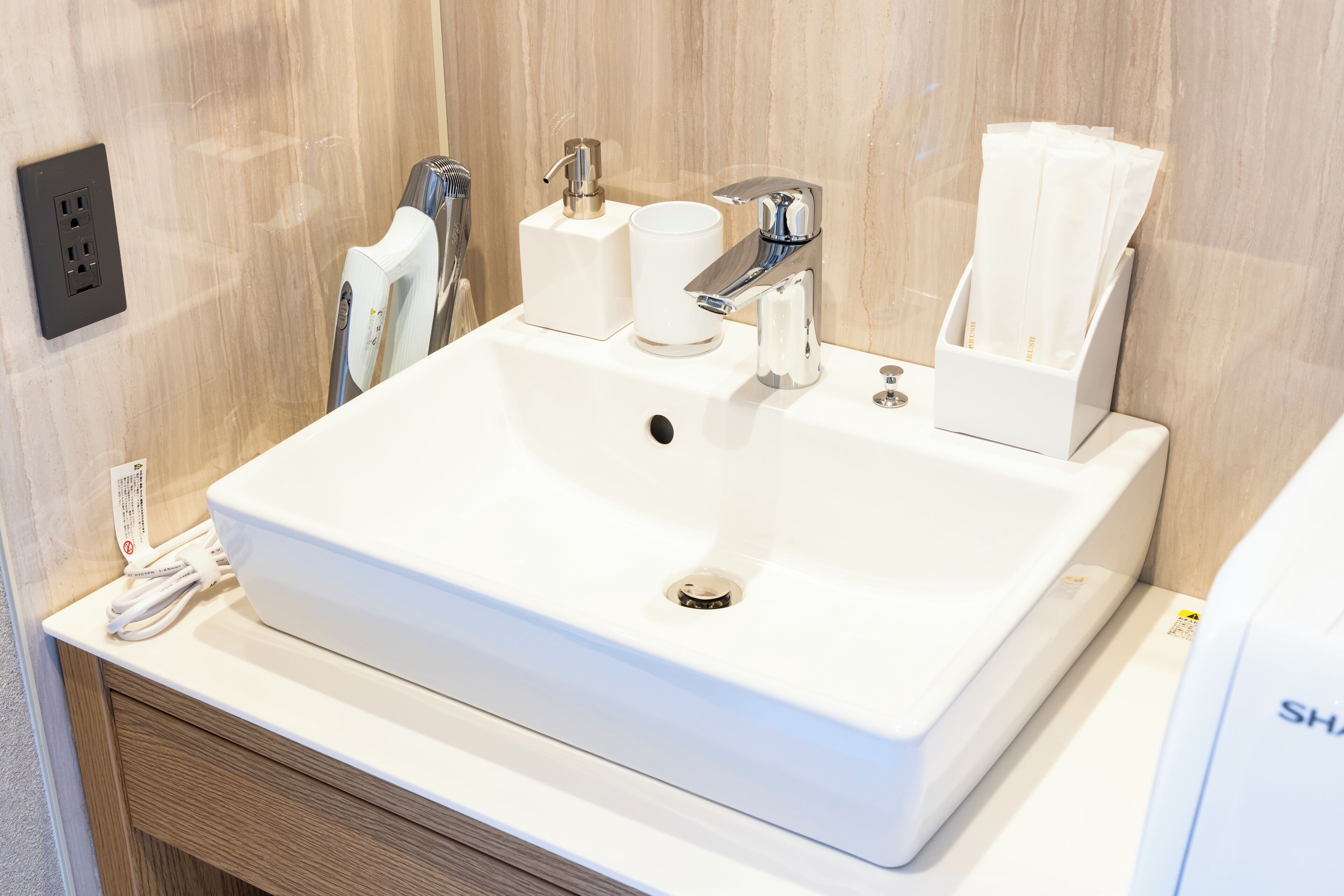 A white bathroom sink with a mirror, a towel dispenser, and a soap dispenser.