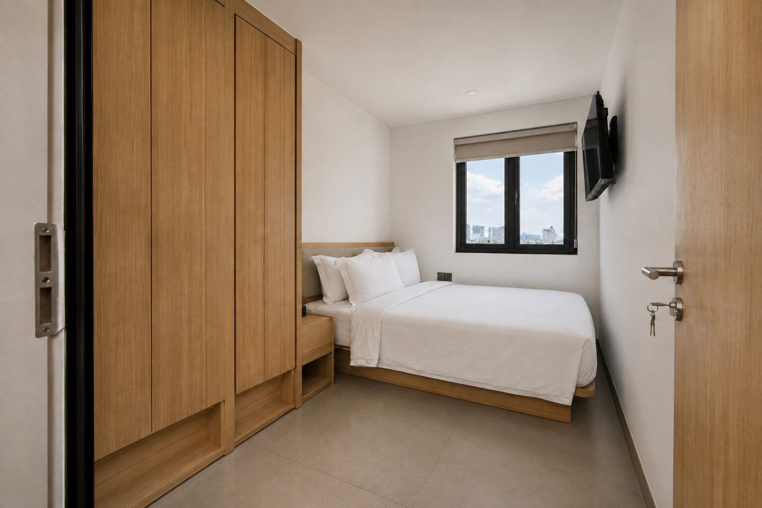 A bedroom with a bed, a nightstand, a wardrobe, and a window with a city view.