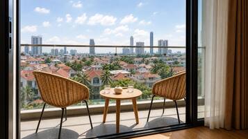 A balcony with two wicker chairs and a small round table, overlooking a cityscape with residential buildings and a clear sky.