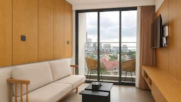 A modern living room with a sofa, chairs, a coffee table, a TV, and a large window with a city view.