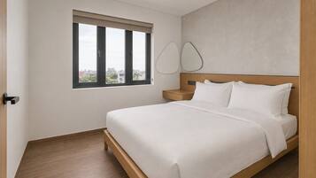 A hotel room with a bed, a nightstand, a window with blinds, and a view of the cityscape.