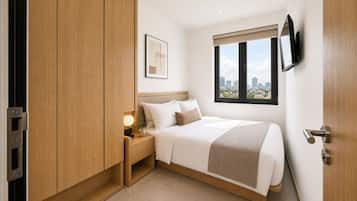 Ein Hotelzimmer mit Bett, Nachttisch, Lampe und Blick auf die Stadt durch das Fenster.