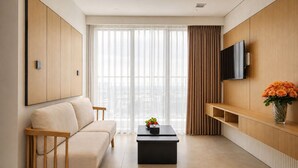 Una sala de estar moderna con sofá, mesa de centro, televisor y vistas amplias a través de grandes ventanales.