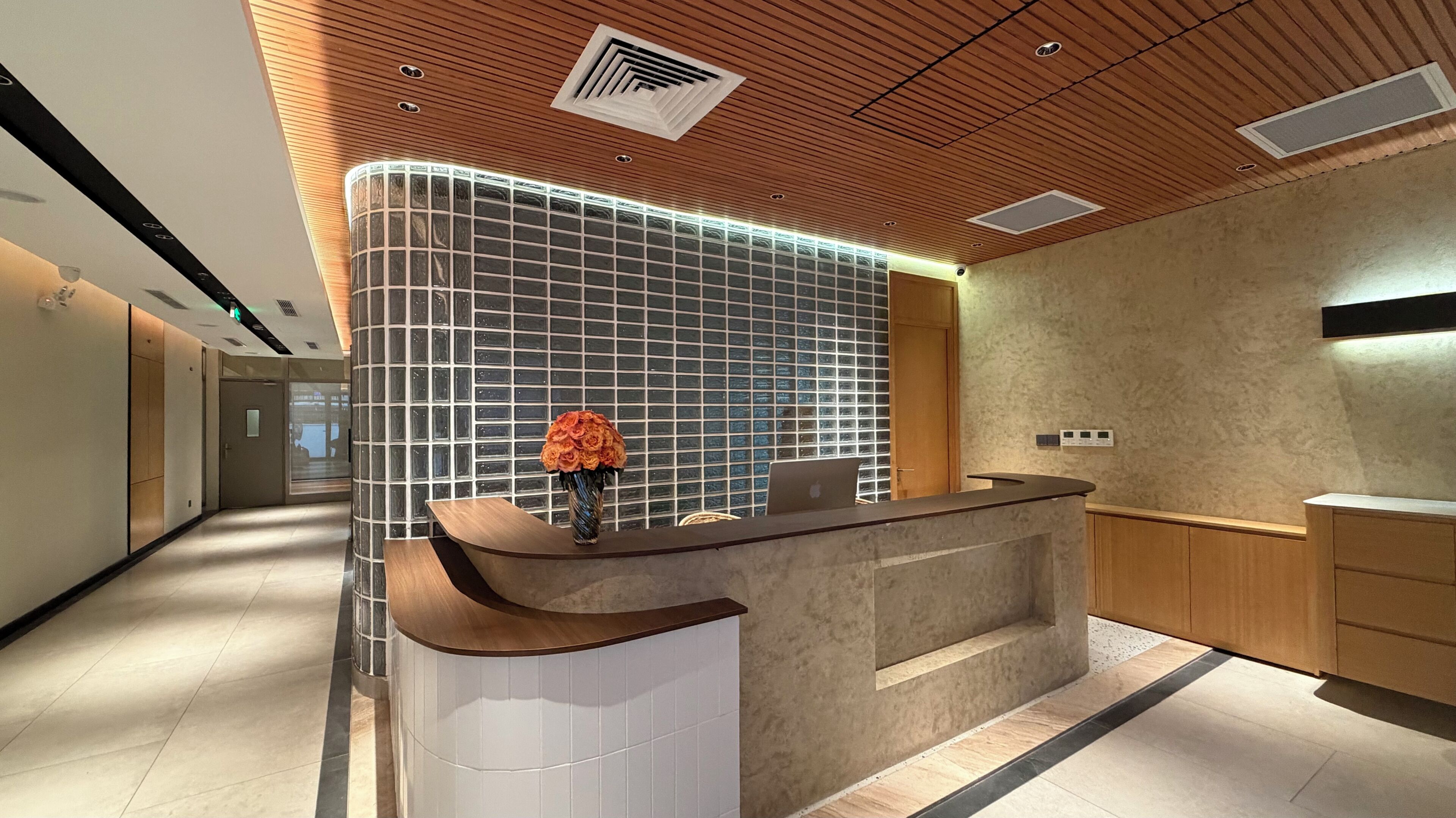 A modern reception desk with a curved design, a vase with flowers, and a laptop.