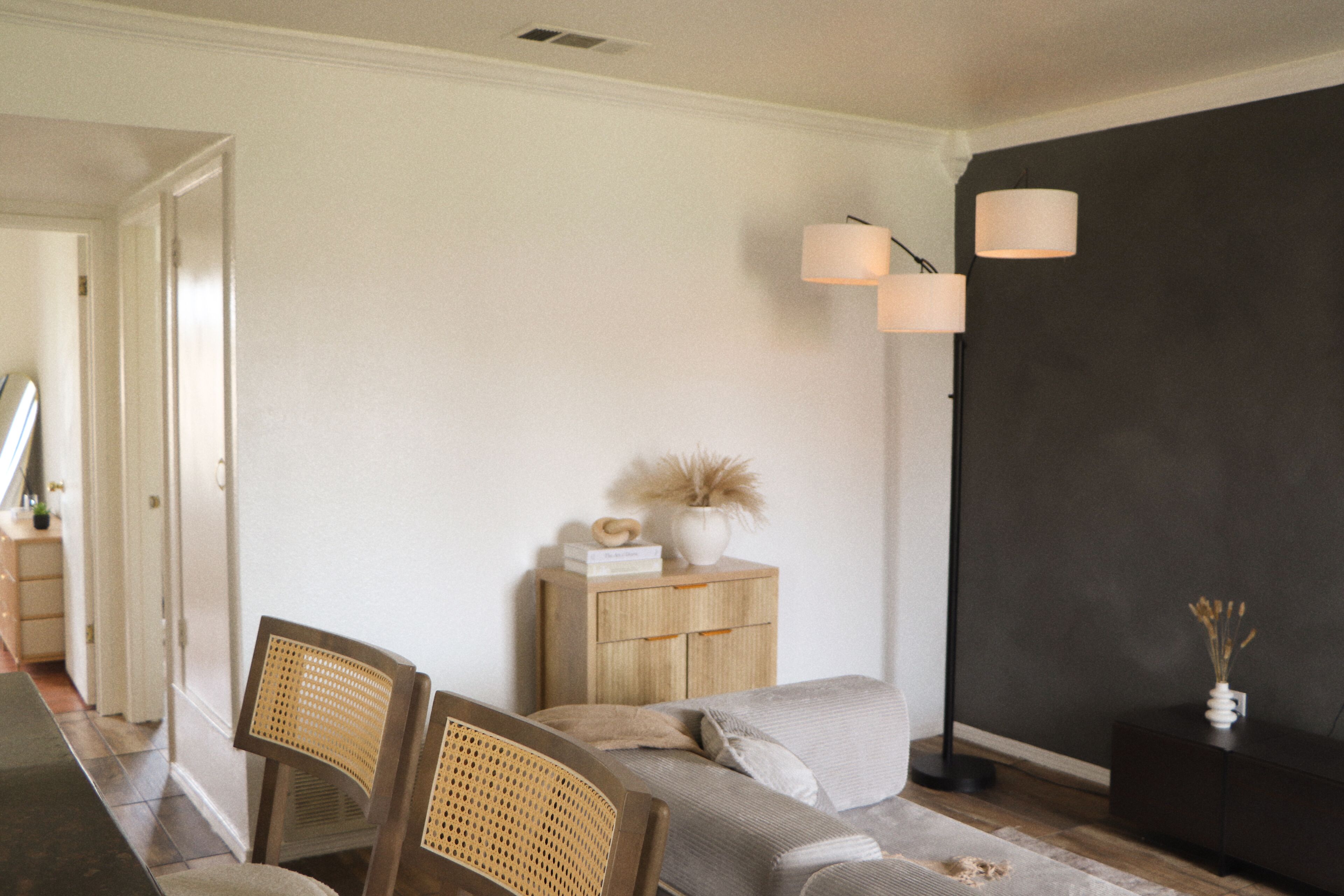 Een moderne woonkamer met een bank, twee houten stoelen, een bijzettafeltje met decoratieve objecten, en een donkere accentmuur.