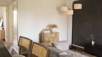 Een moderne woonkamer met een bank, twee houten stoelen, een bijzettafeltje met decoratieve objecten, en een donkere accentmuur.