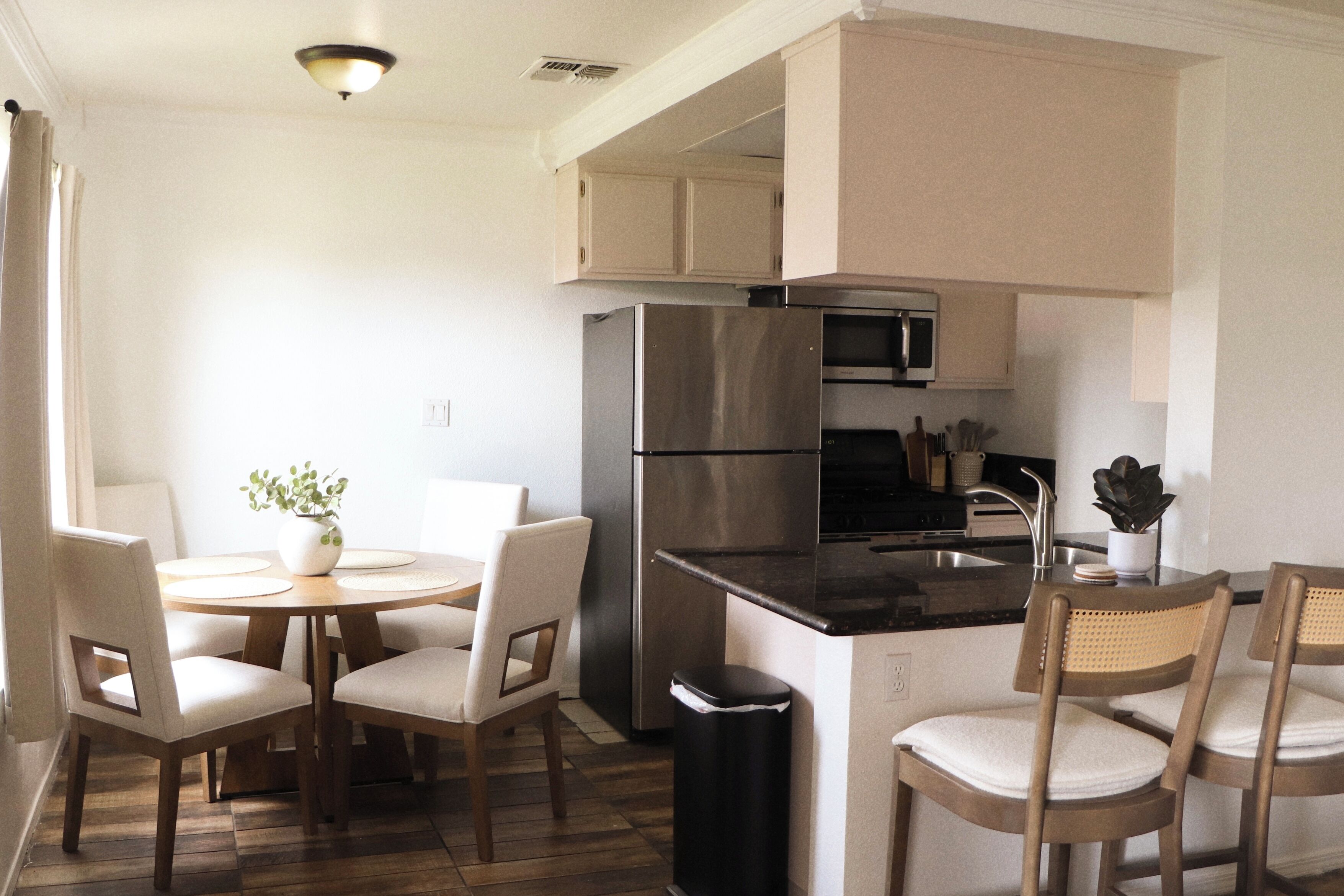 A modern kitchen with a stainless steel refrigerator, a microwave, and a sink. There is a dining area with a round table and chairs.