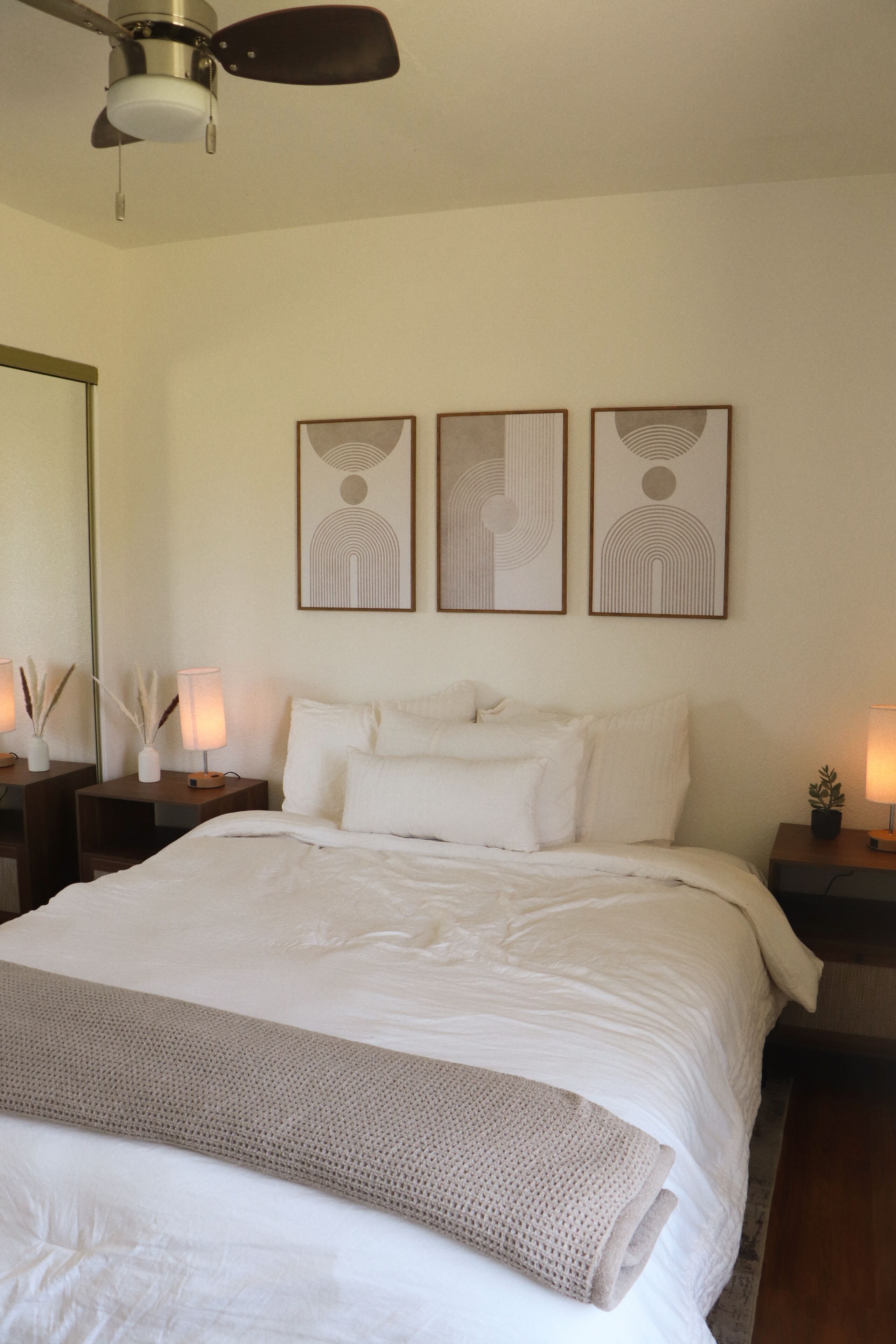 A bedroom with a bed, bedside tables, lamps, and wall art.