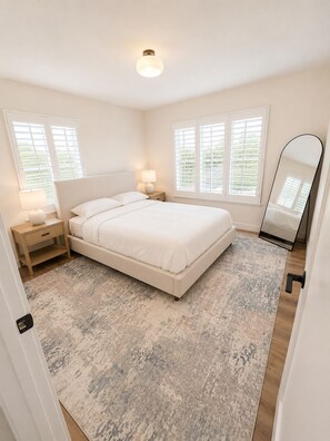 A bedroom with a bed, bedside tables, a nightstand, a mirror, and windows. - Cozy Inglewood retreat (Vernon)
