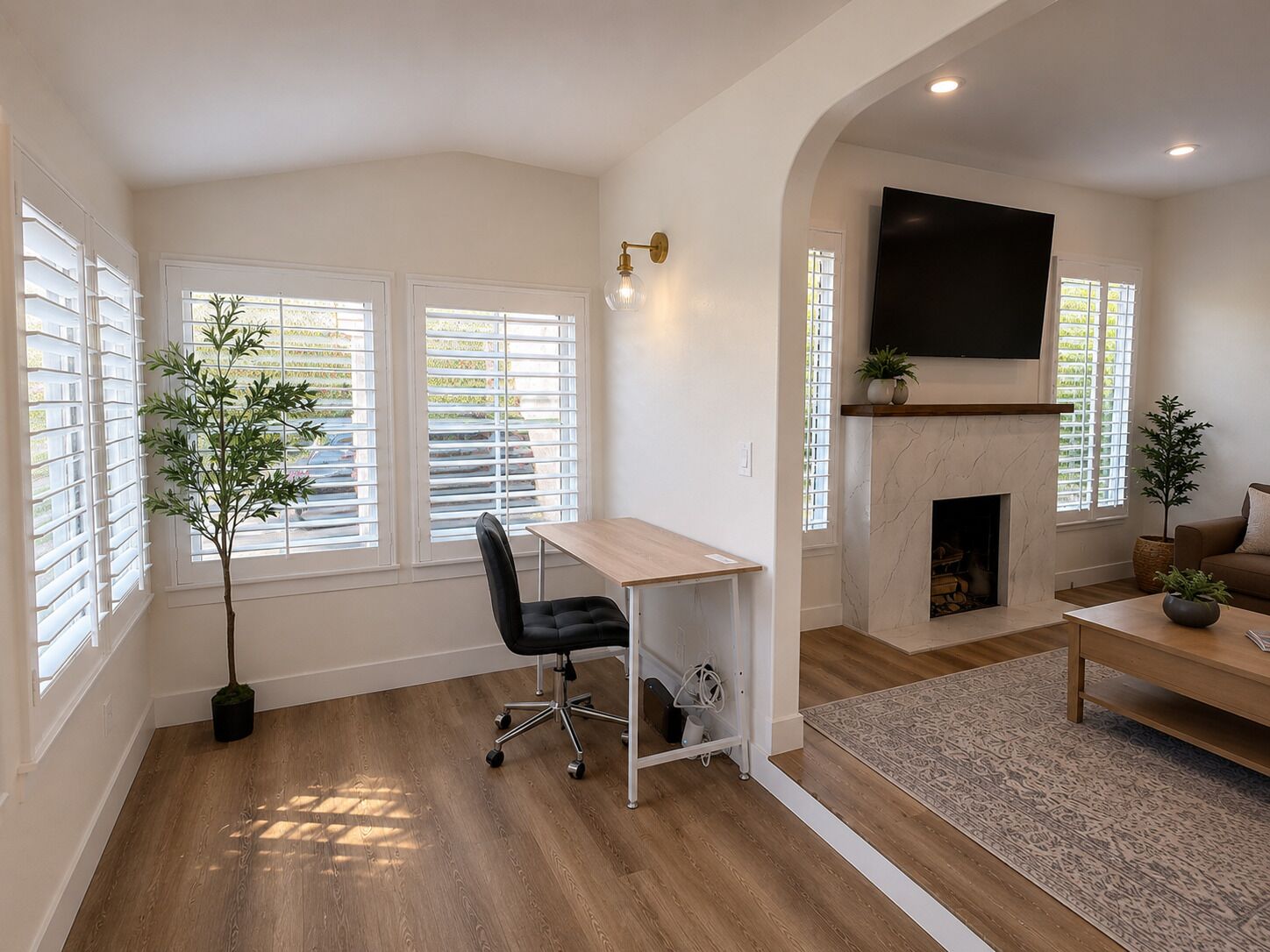 A modern living room with a fireplace, a flat-screen TV mounted above it, and a desk with a chair.