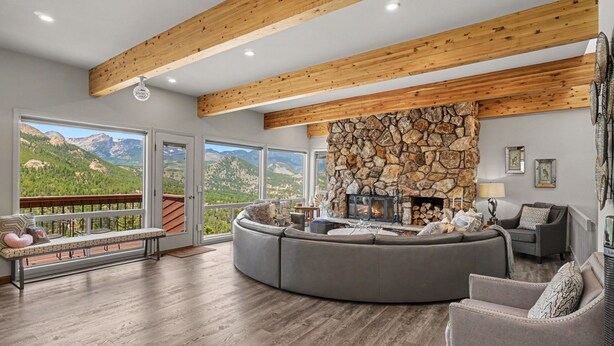 A spacious living room with a stone fireplace, large windows offering mountain views, and a wooden ceiling. - Trail's End - 22-zone3197 3 Bedroom Condo (Estes Park)