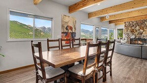 A dining area with a wooden table and chairs, large windows with mountain views, and a stone fireplace. - Trail's End - 22-zone3197 3 Bedroom Condo (Estes Park)