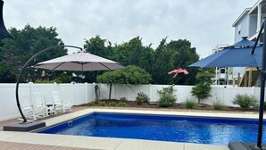 A swimming pool with a wooden deck, two umbrellas, and a white fence. - Live Oaks / 127 Ocean Blvd East 4 Bedroom Home (Supply)