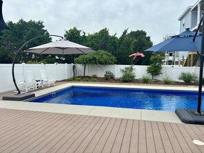 Ein Schwimmbecken mit Holzterrasse, zwei Sonnenschirmen und einem weißen Zaun.