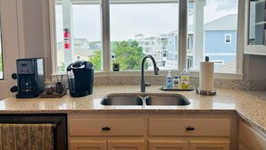 A kitchen with a double sink, a coffee maker, and a window with a view of neighboring houses. - Live Oaks / 127 Ocean Blvd East 4 Bedroom Home (Supply)