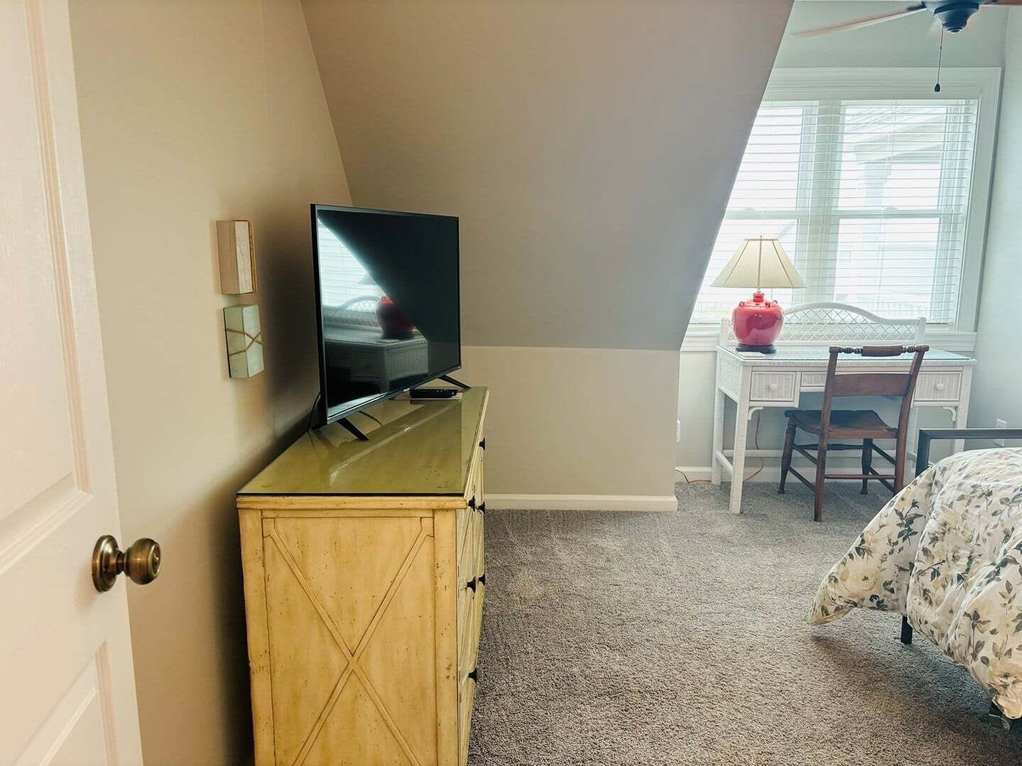 A bedroom with a television on a dresser, a desk with a lamp, and a bed with a floral bedspread.
