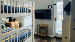 A room with bunk beds, a television, a small table, and a door with a window. - Live Oaks / 127 Ocean Blvd East 4 Bedroom Home (Supply)