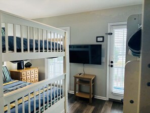 Ein Zimmer mit Etagenbetten, einem Fernseher, einem kleinen Tisch und einer Tür mit Fenster.