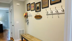 A hallway with a wooden bench, wall-mounted hooks, and framed artwork. - Live Oaks / 127 Ocean Blvd East 4 Bedroom Home (Supply)