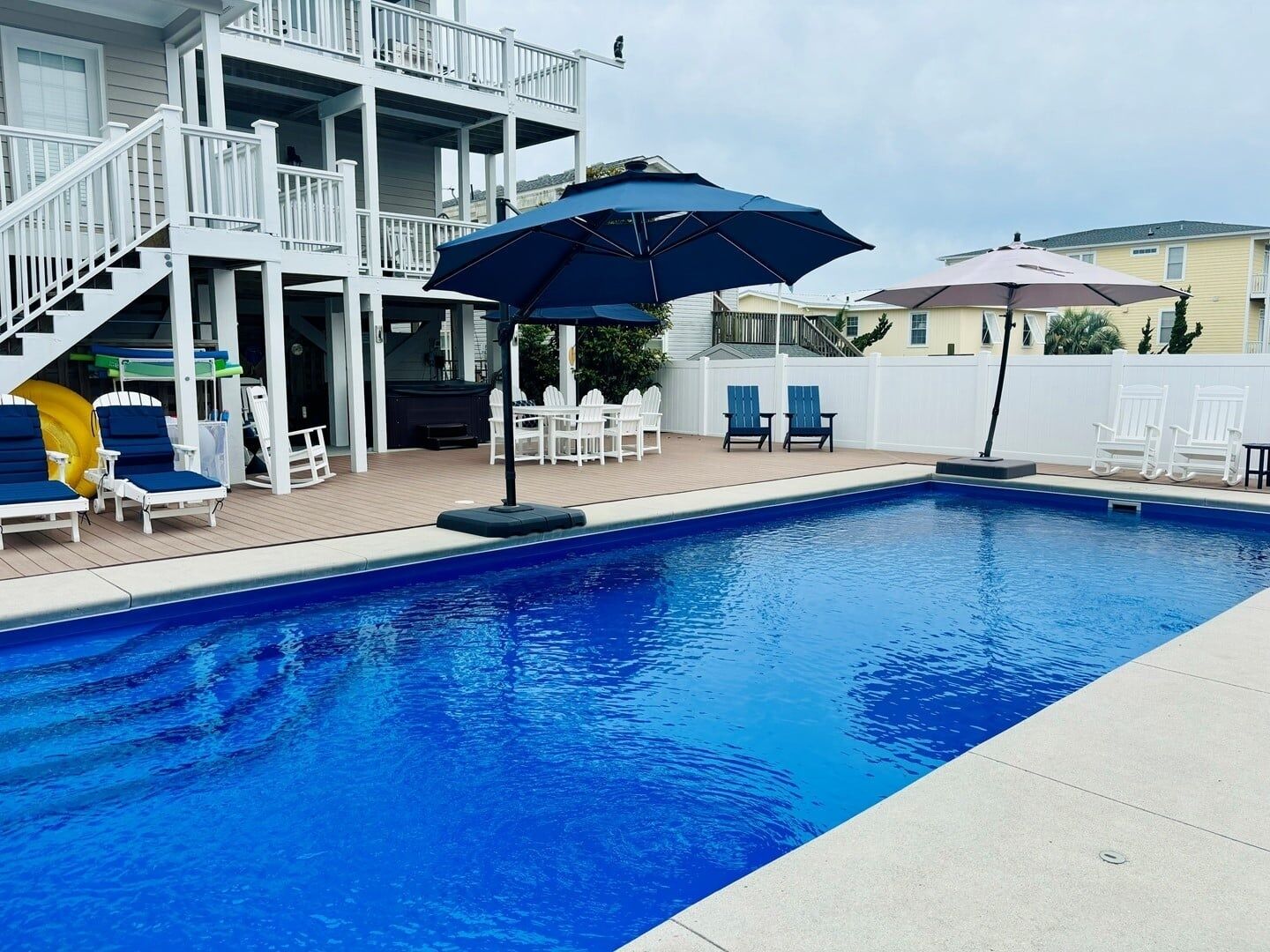 A swimming pool with lounge chairs and umbrellas, a covered deck area, and a multi-level building with a white exterior.