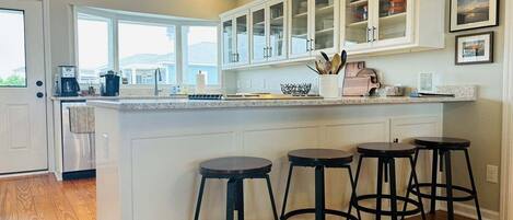A kitchen with a central island, bar stools, and a view of the outdoors.