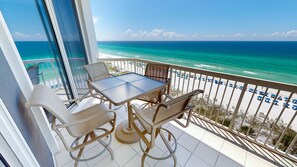 Ein Balkon mit Tisch und Stühlen mit Blick auf einen Strand mit Sonnenschirmen.