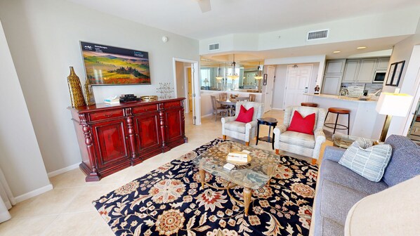 A living room with a large flat-screen TV, a red wooden cabinet, a patterned rug, and a glass coffee table. - Silver Beach 0902e 2 Bedroom Condo (Destin)