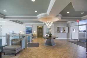 Eine großzügige Lobby mit hoher Decke, einem zentralen Kronleuchter, einer Sitzecke mit einer Couch und Sesseln sowie einem Empfangstresen.