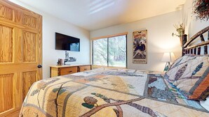 A bedroom with a large bed, a wooden wardrobe, a television on the wall, and a window with blinds. - Seasons 4 #104 2 Bedroom Condo (Mammoth Lakes)