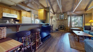 A cozy living area with a stone fireplace, wooden bar stools, and a large flat-screen TV. - Seasons 4 #104 2 Bedroom Condo (Mammoth Lakes)