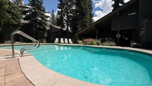 A swimming pool with a metal ladder, surrounded by lounge chairs and a building with a dark exterior. - Seasons 4 #104 2 Bedroom Condo (Mammoth Lakes)
