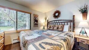 A bedroom with a large bed, a window with blinds, a wall-mounted lamp, and a decorative wreath. - Seasons 4 #104 2 Bedroom Condo (Mammoth Lakes)