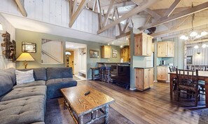 A spacious living area with a sofa, a coffee table, and a kitchen with wooden cabinets and a dining area. - Seasons 4 #104 2 Bedroom Condo (Mammoth Lakes)