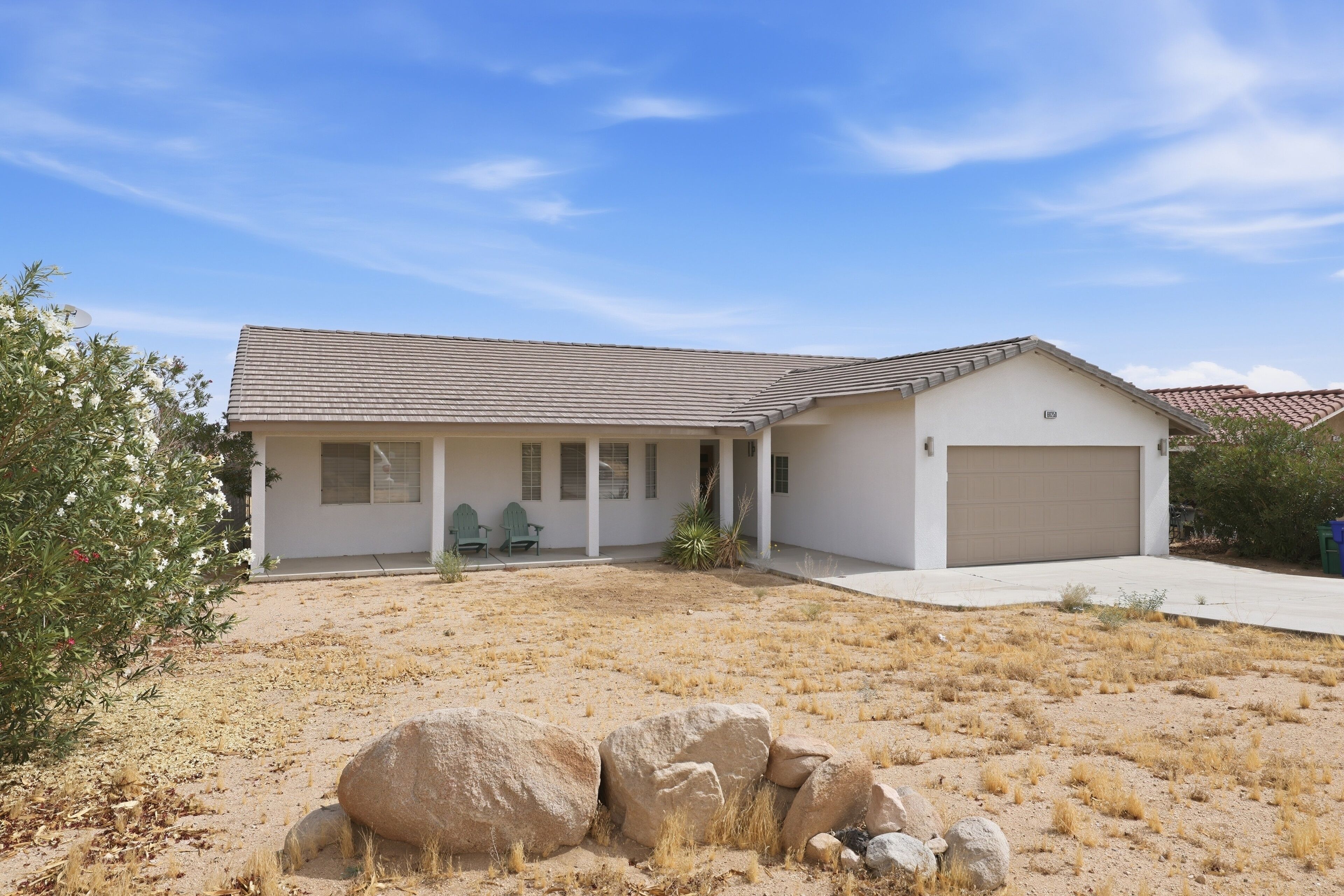 A single-story house with a covered porch, a garage, and a dry, rocky yard.