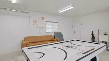 A room with a white table hockey table, a brown sofa, a window with blinds, and a wall with a 'Villa Soleil' sign.