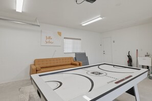 A room with a white table hockey table, a brown sofa, a window with blinds, and a wall with a 'Villa Soleil' sign. - Joshua Tree El Oasis 3br Retreat For 6 Guests 3 Bedroom Home (Joshua Tree)
