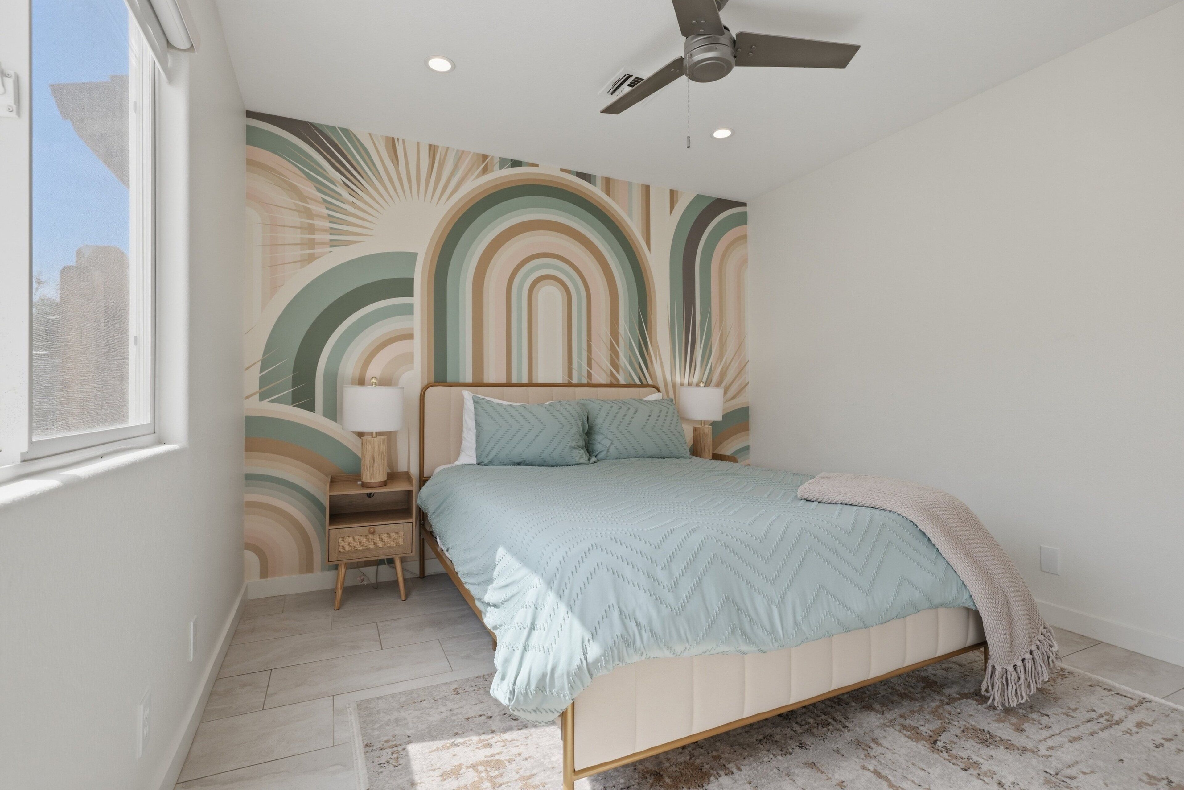A bedroom with a bed, nightstands, a ceiling fan, and a wall with a geometric pattern.