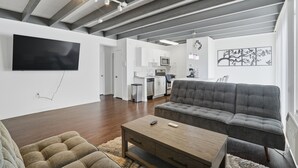A modern living room with a grey sofa, a wooden coffee table, and a flat-screen TV mounted on the wall. - Quiet Flat Near Philly - Full Chef's Kitchen 1 Bedroom Apts (Glenolden)