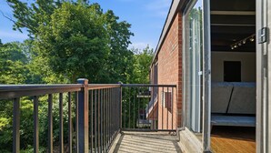 A balcony with a metal railing, a brick building, and a view of trees. - Quiet Flat Near Philly - Full Chef's Kitchen 1 Bedroom Apts (Glenolden)