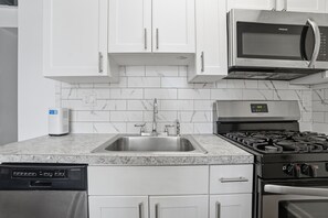A kitchen with white cabinets, a stainless steel sink, a microwave, a dishwasher, and a stove.