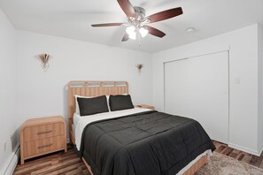 A bedroom with a bed, wooden nightstands, a ceiling fan, and a white door.