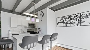 A modern kitchen with white cabinets, a central island with bar stools, a microwave, and a clock on the wall. - Quiet Flat Near Philly - Full Chef's Kitchen 1 Bedroom Apts (Glenolden)
