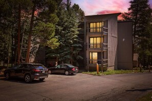 A modern building with a two-story structure, a parking area with two cars, and a forested background. - Gold Camp F97 2 Bedroom Condo (Breckenridge)