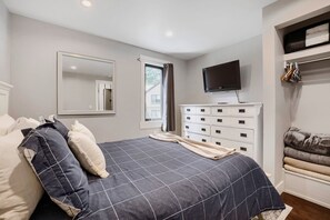 Ein Schlafzimmer mit Bett, Kommode, Fernseher und Fenster.