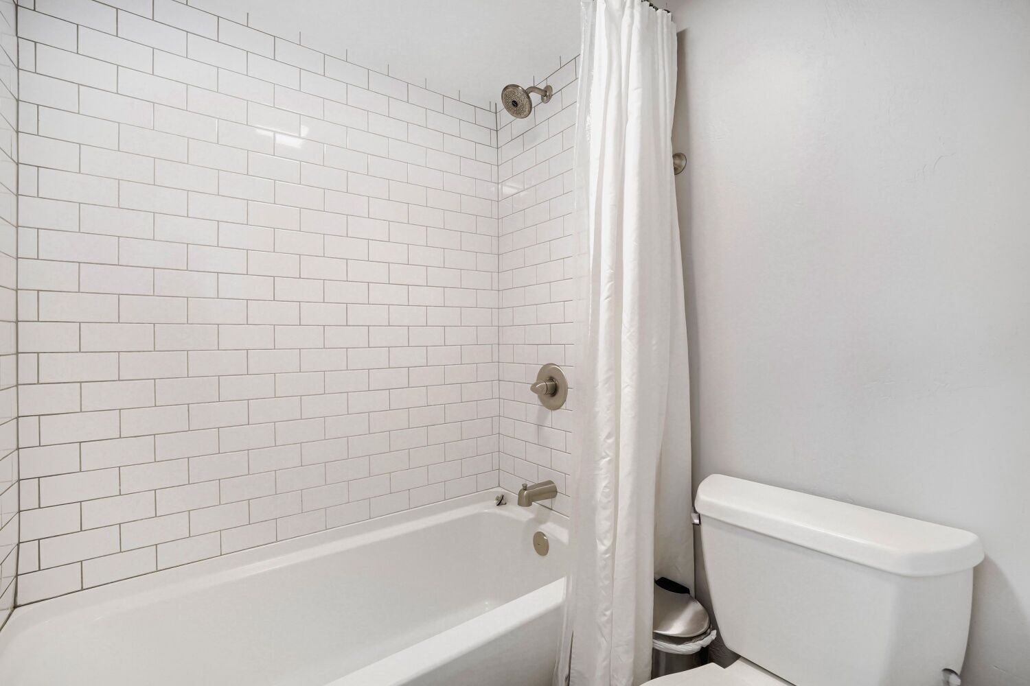Une salle de bain avec des carreaux de céramique blancs rectangulaires, une baignoire et des toilettes.