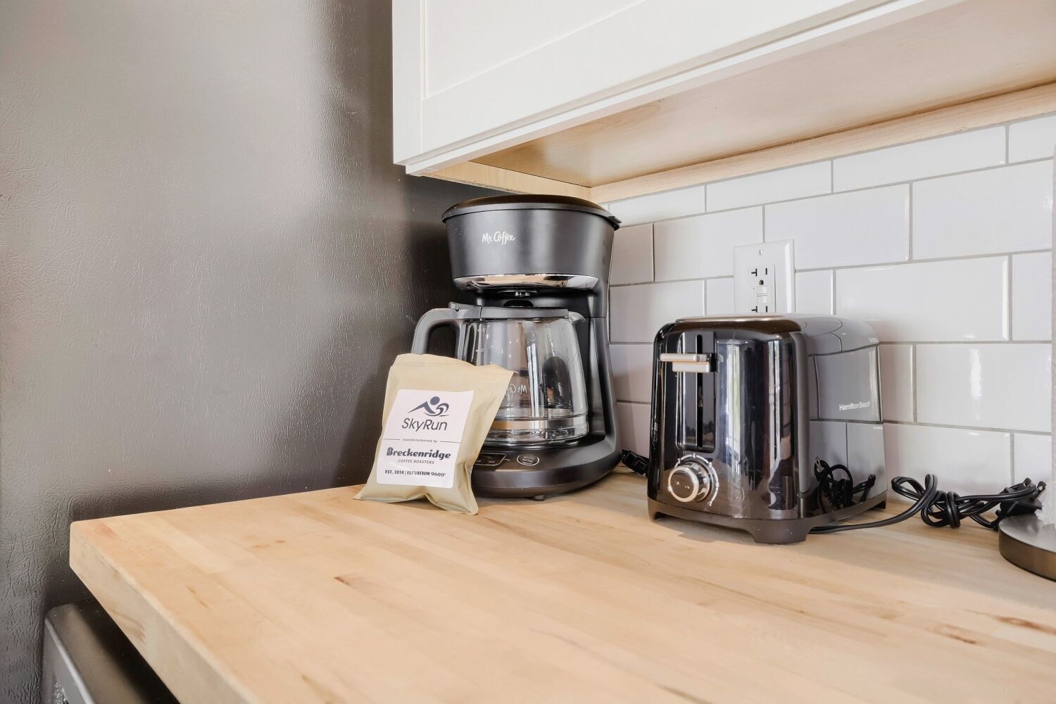 A kitchen counter with a coffee maker, a bag of coffee, and a toaster.