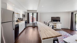Una cucina moderna con isola centrale, zona pranzo con un tavolo lungo e televisione nella zona living.
